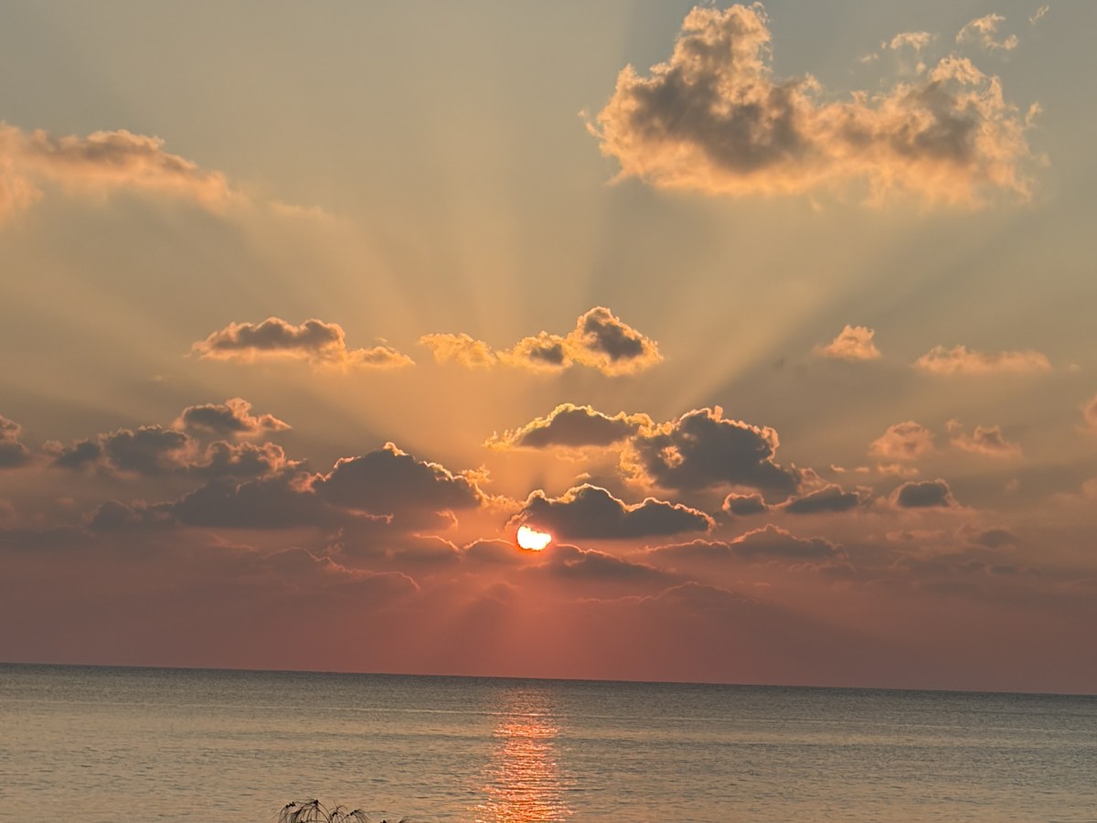 Sunburst rays fan across the sea at sunset off Coral Sunset
